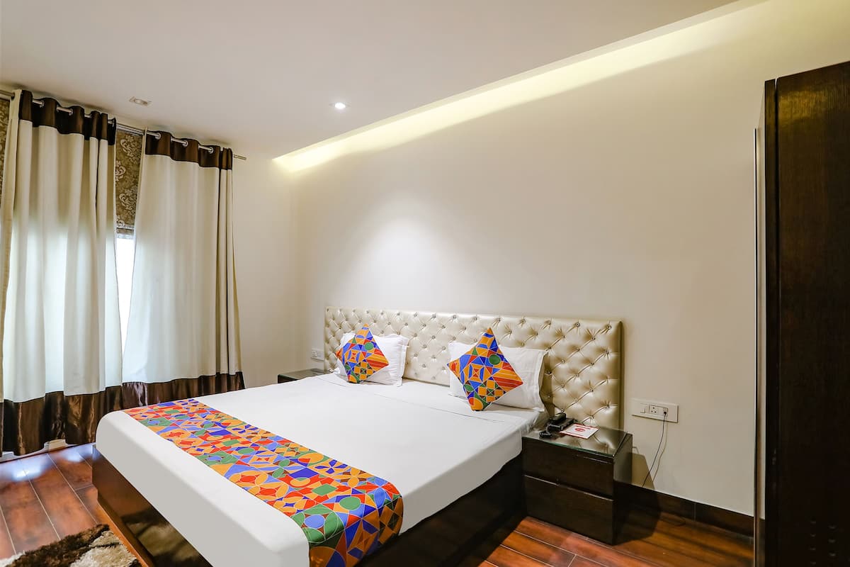 A hotel room with a large bed, a nightstand, a bedside table, and a window with curtains.
