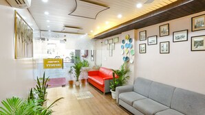 A reception area with a red and grey sofa, potted plants, and framed pictures on the walls. - FabHotel Delta Suites I (New Delhi)