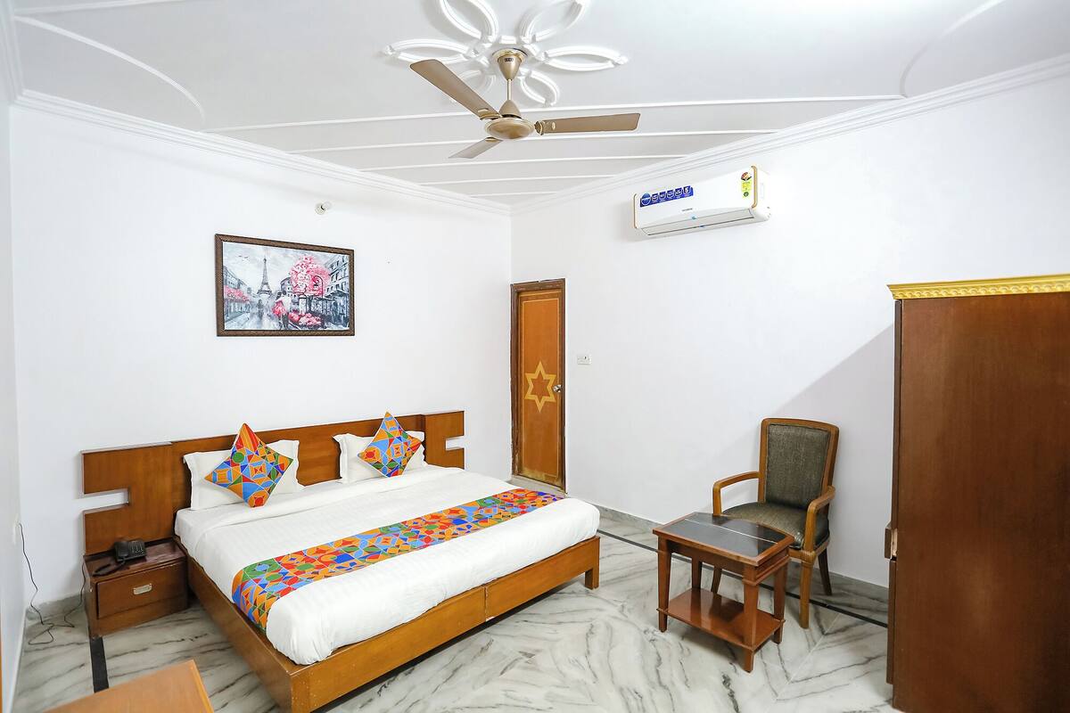 A hotel room with a bed, a chair, a wardrobe, a ceiling fan, an air conditioning unit, and a framed picture on the wall.