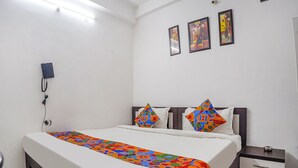 Ein Hotelzimmer mit einem Bett, einem Nachttisch mit Schubladen, einem Telefon an der Wand und drei gerahmten Bildern an der Wand.