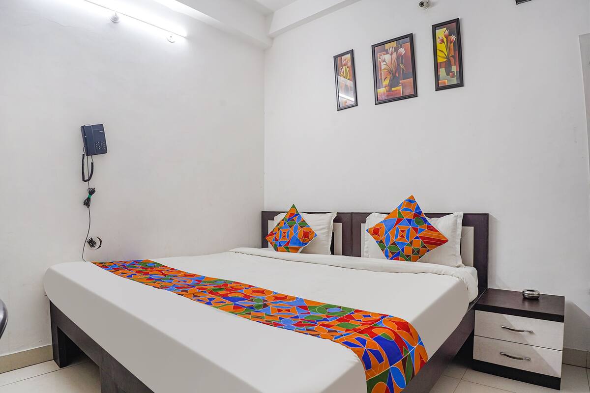 A hotel room with a bed, a bedside table with drawers, a telephone on the wall, and three framed pictures on the wall.