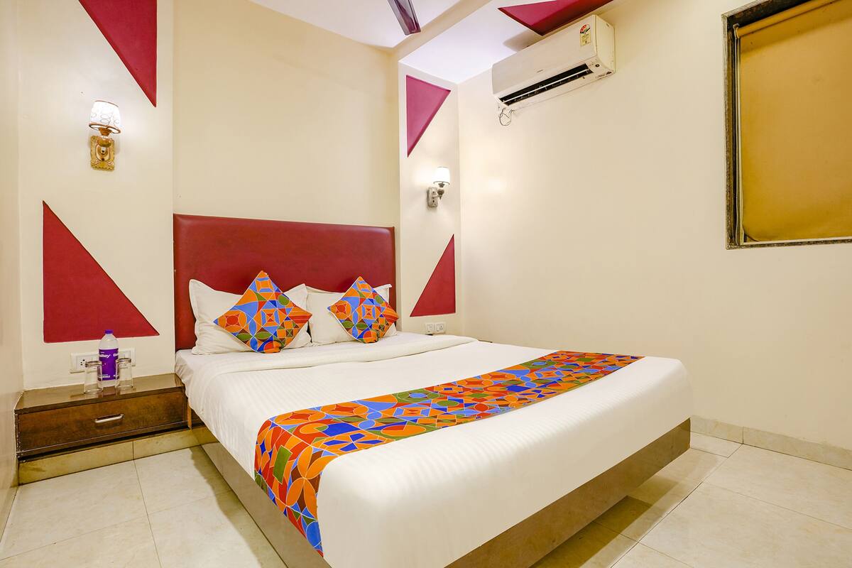 A hotel room with a large bed, red geometric wall decorations, and a colorful bedspread.