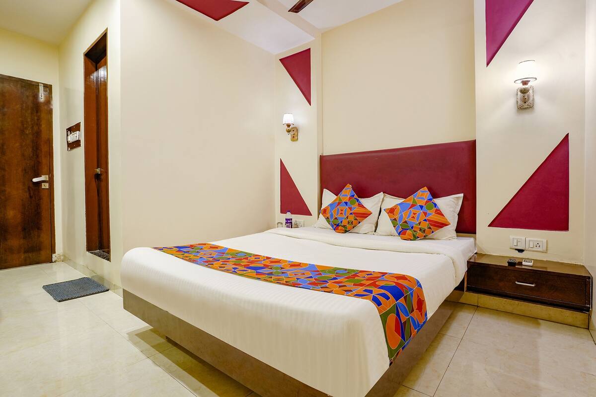 A hotel room with a bed, nightstand, wall-mounted light, and a door.