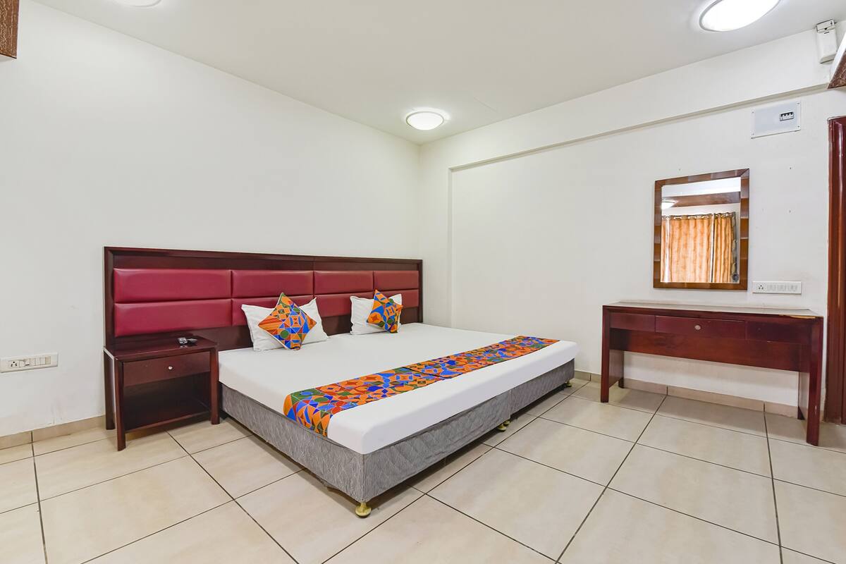 Une chambre d’hôtel bien rangée, avec un grand lit, une table de chevet, un bureau en bois et un miroir au mur.