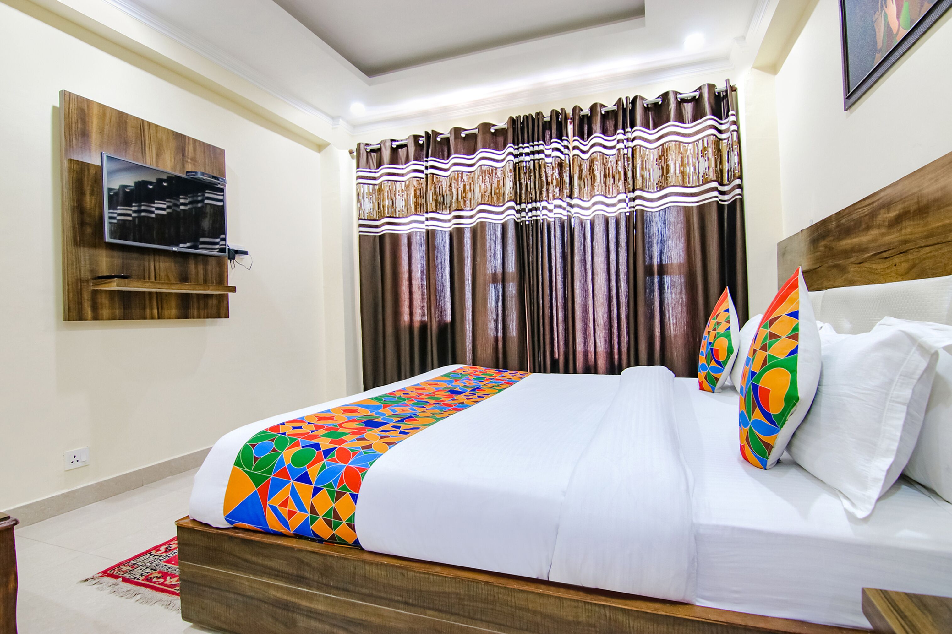Una habitación de hotel con una cama, un televisor montado en la pared y cortinas.