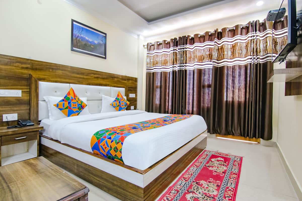 A hotel room with a wooden headboard, a bed with colorful pillows, a red patterned rug, and a large window with curtains.