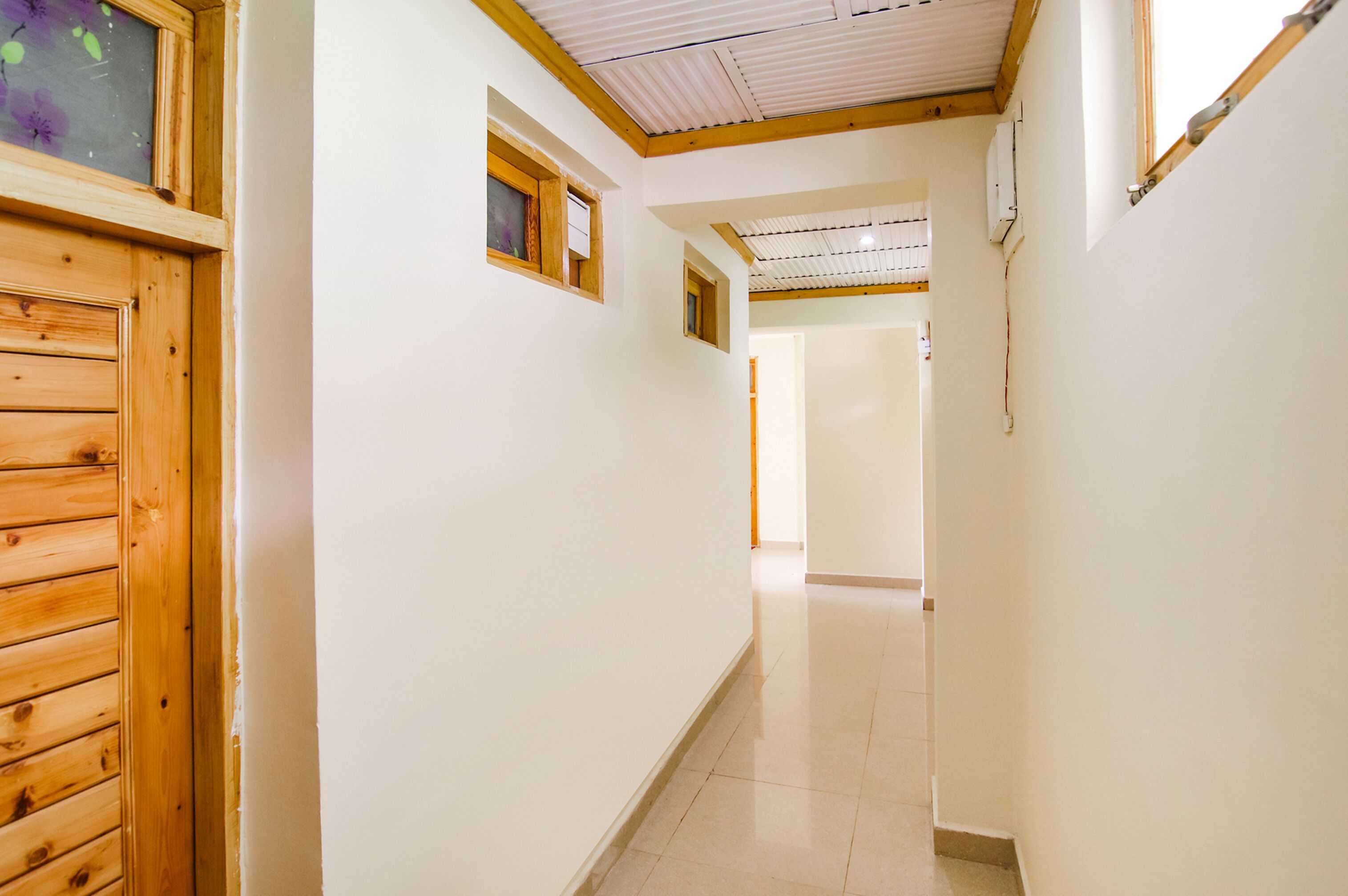 A hallway with wooden doors and windows, leading to a room with a tiled floor and a ceiling with wooden beams.