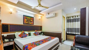 A hotel room with a bed, bedside tables, a chair, a ceiling fan, an air conditioning unit, and a painting on the wall. - Fabhotel Sairam Residency (Bengaluru)