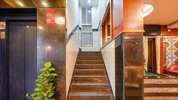 A staircase with a surveillance sign, a potted plant, and a door with a geometric pattern. - Fabhotel Sairam Residency (Bengaluru)