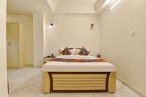 A bedroom with a bed, wooden headboard, bedside table, nightstand, and a wardrobe.
