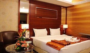 A hotel room with a large bed, two bedside tables, a chair, and a small table with a vase of flowers.