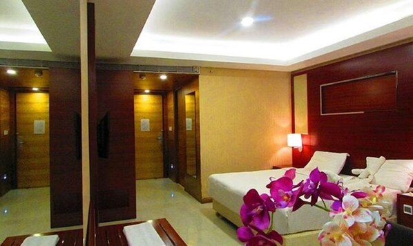 A hotel room with a bed, a desk, a chair, a mirror, and a wall-mounted TV.