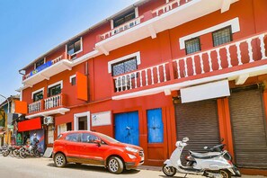 A red building with balconies, a closed shop, and a parked car and scooter. - FabExpress Casa Paradiso (Panaji)
