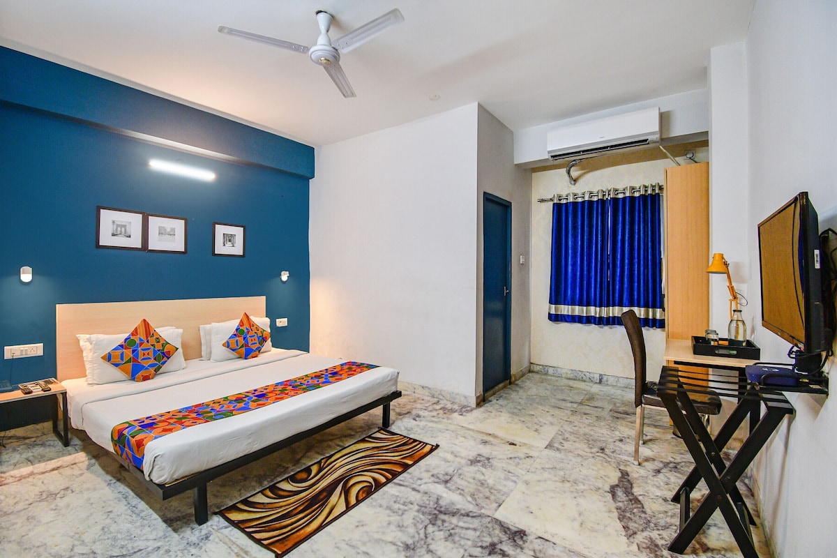 A bedroom with a bed, a desk, a chair, a ceiling fan, and a TV.