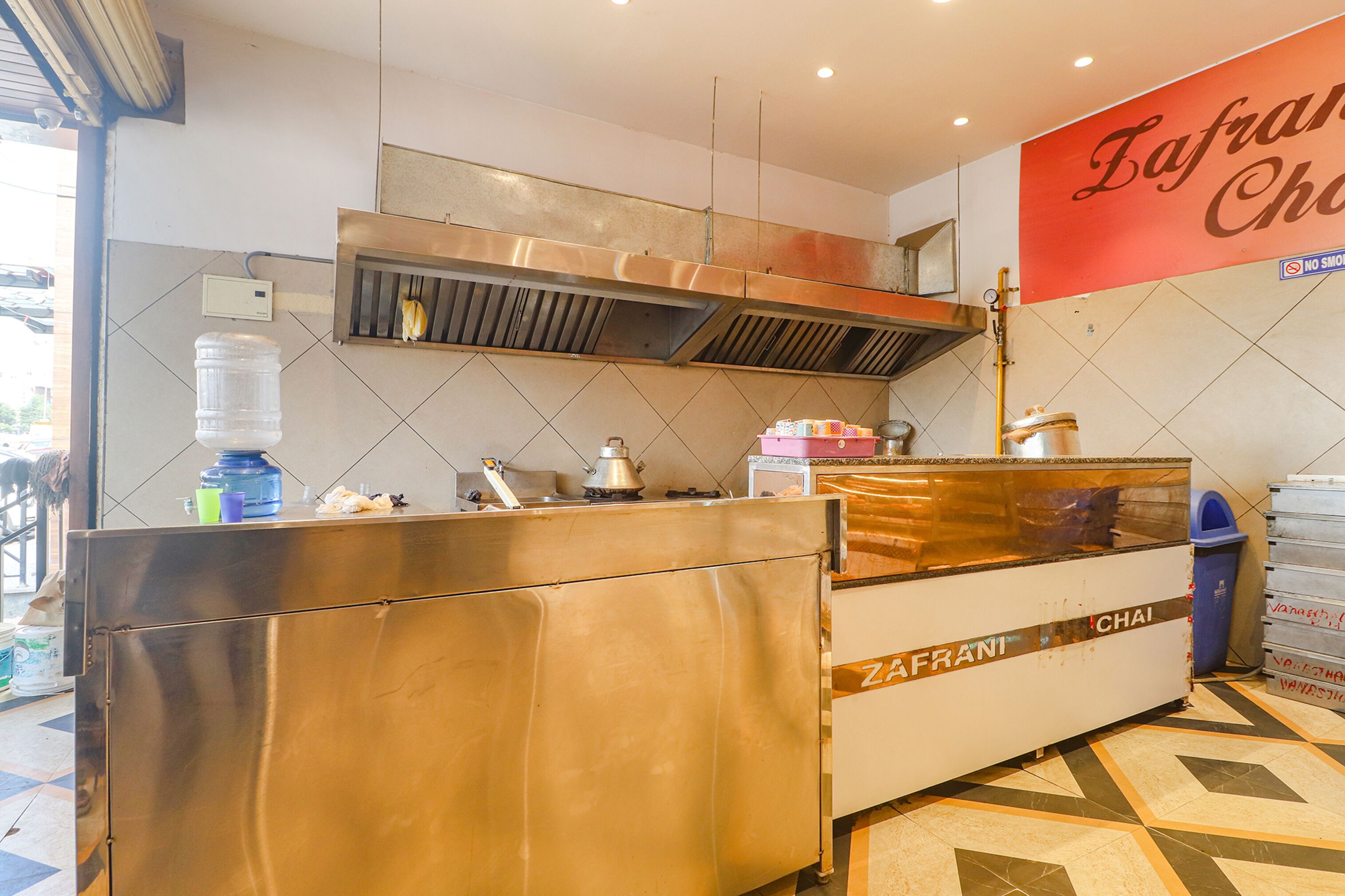 A kitchen area with a stainless steel counter, a water dispenser, and a large red sign with the name "Zafran Chi".