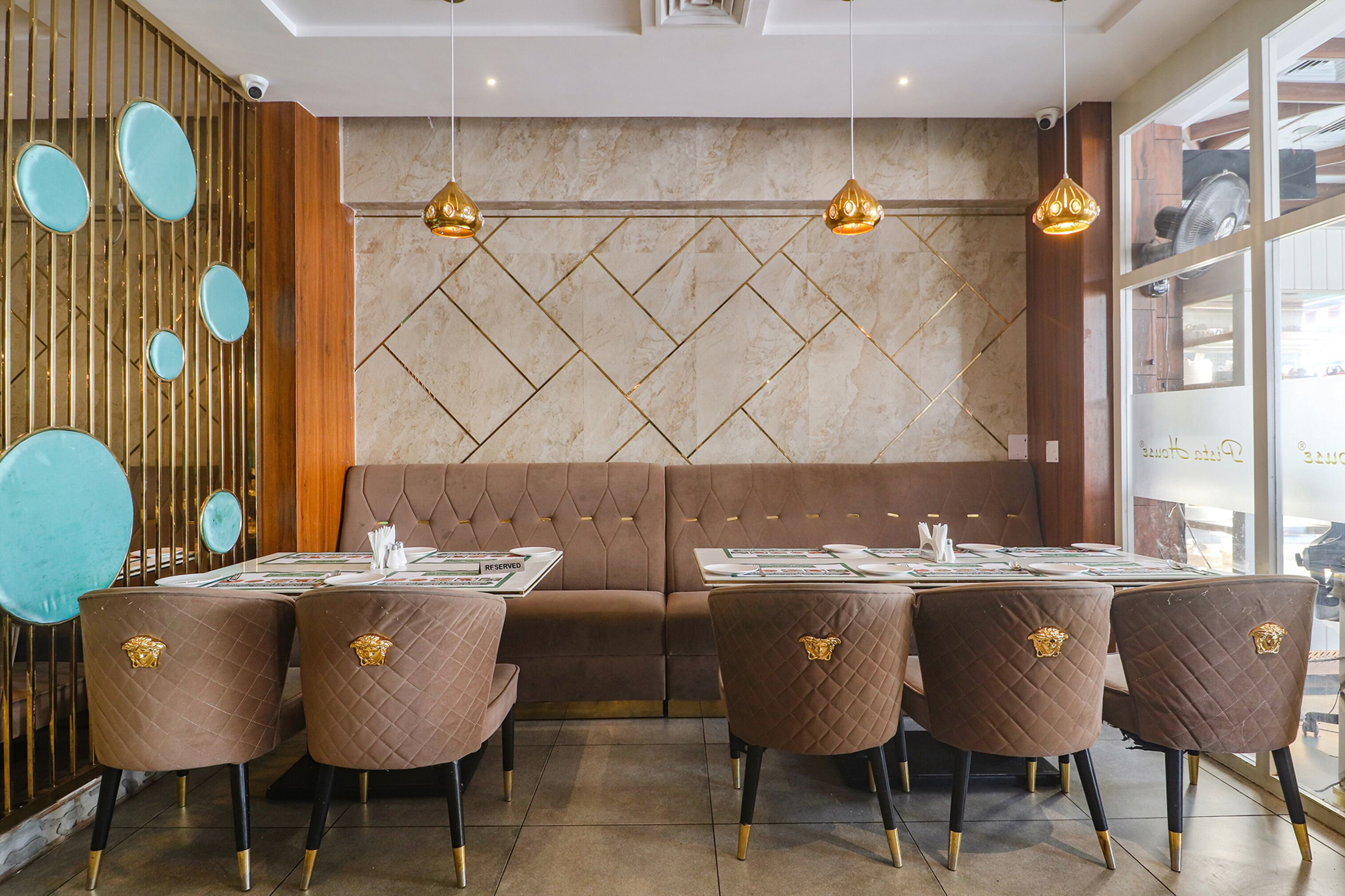 A restaurant with a modern interior, featuring a brown cushioned bench, a table set with a menu, and a decorative wall with geometric patterns.