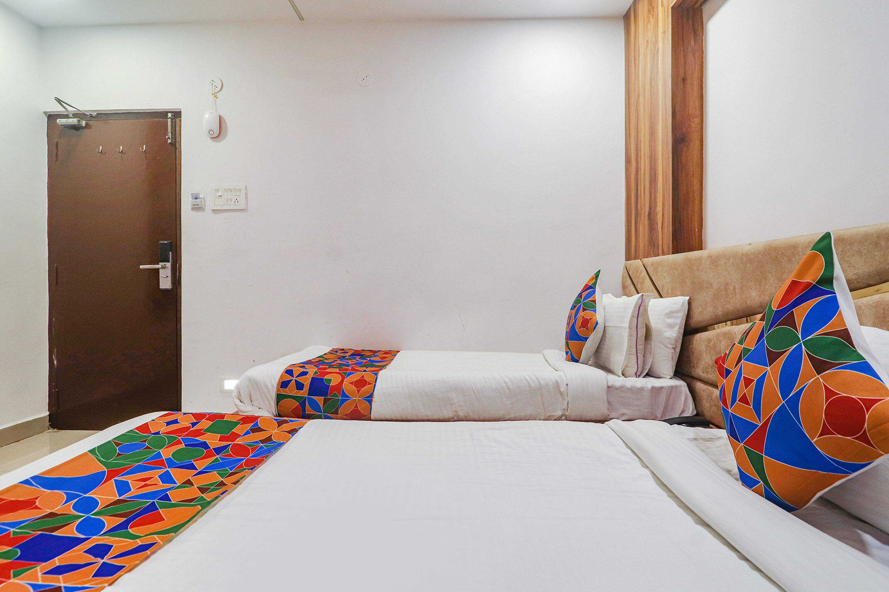 A hotel room with a bed, a smaller bed, a wooden door, and a window with curtains.