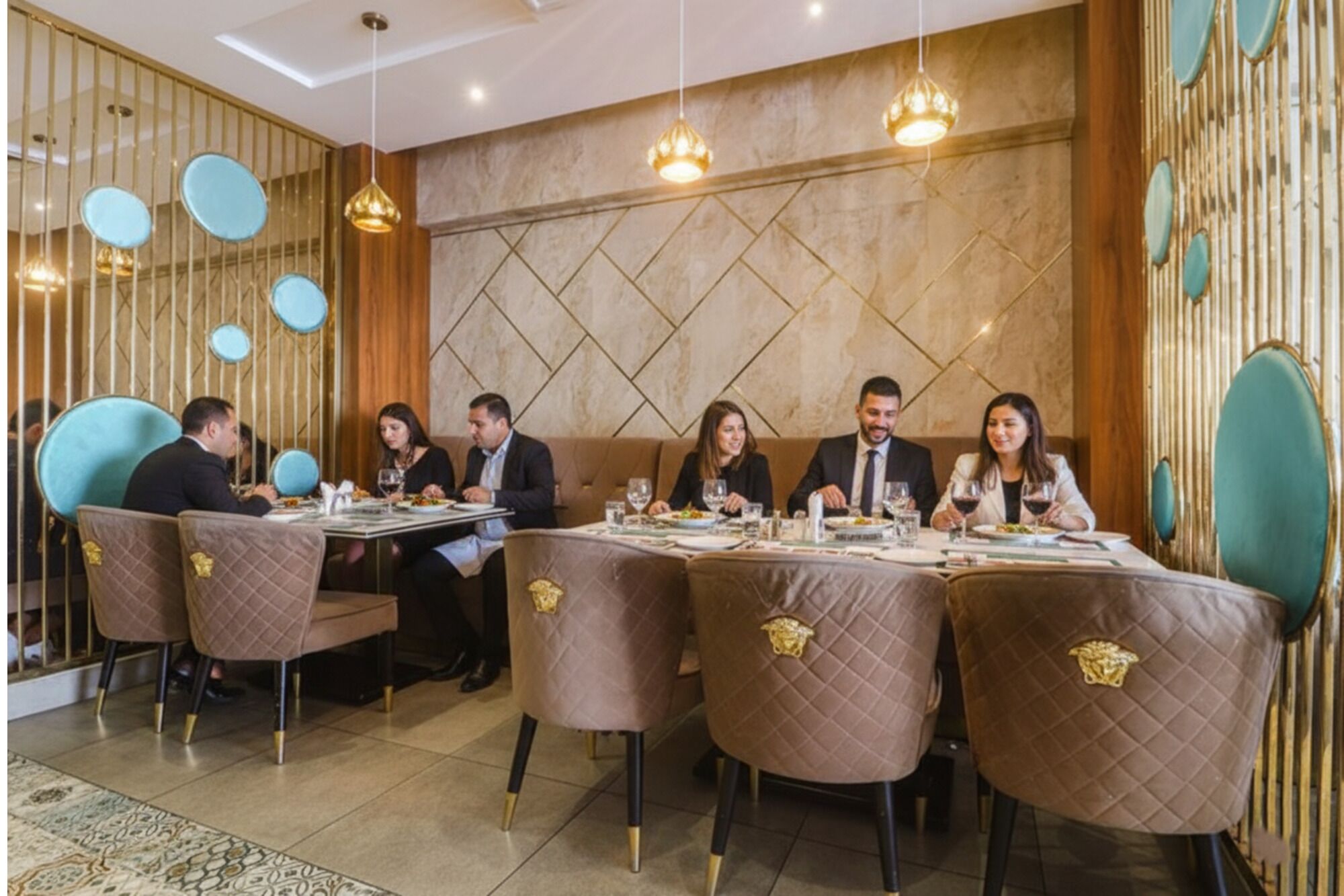 A restaurant with a modern interior, featuring a long table with six chairs, each with a quilted pattern and gold accents.