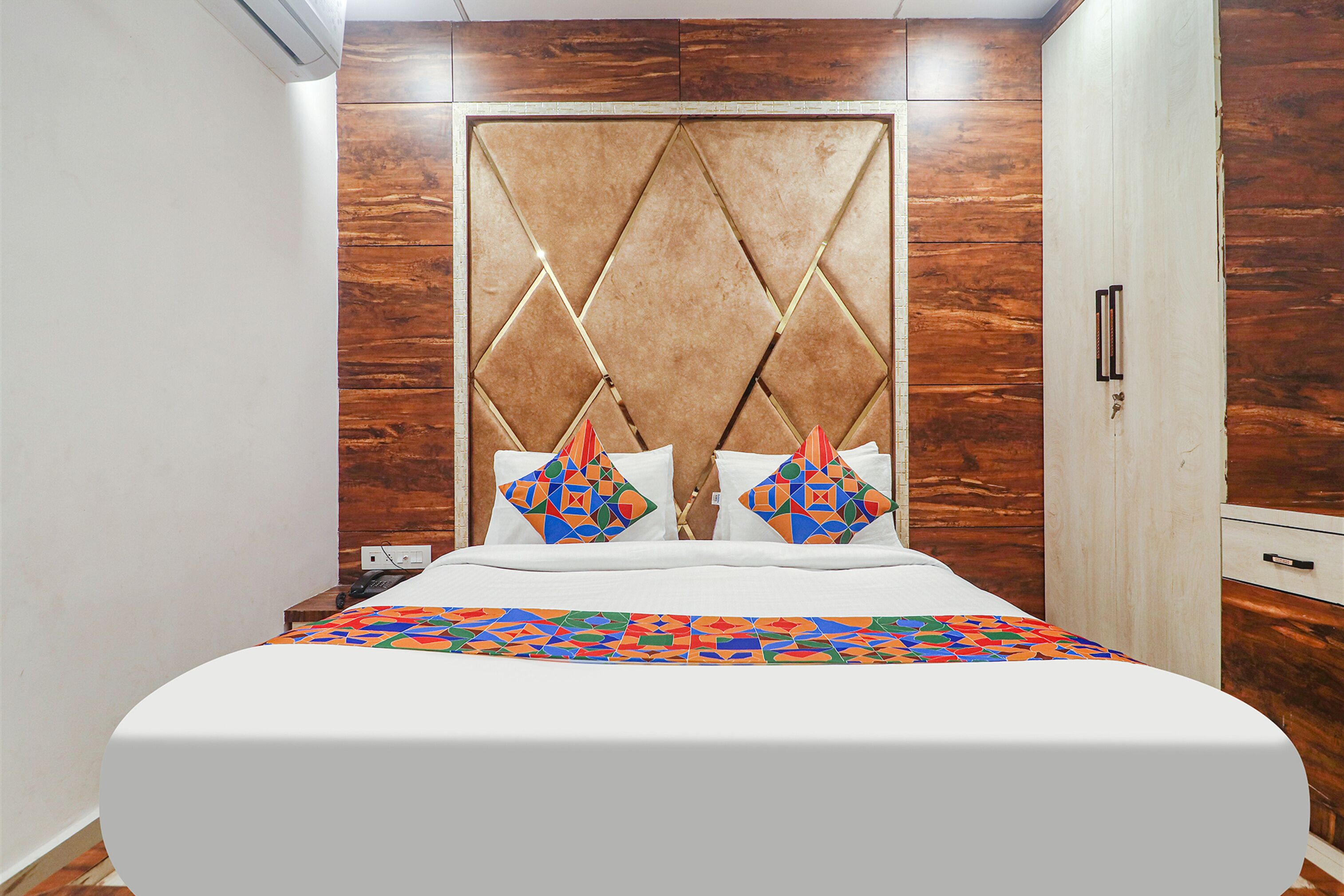 A neatly made bed with a colorful geometric-patterned bedspread, a wooden headboard with a diamond pattern, and two pillows with a geometric design.