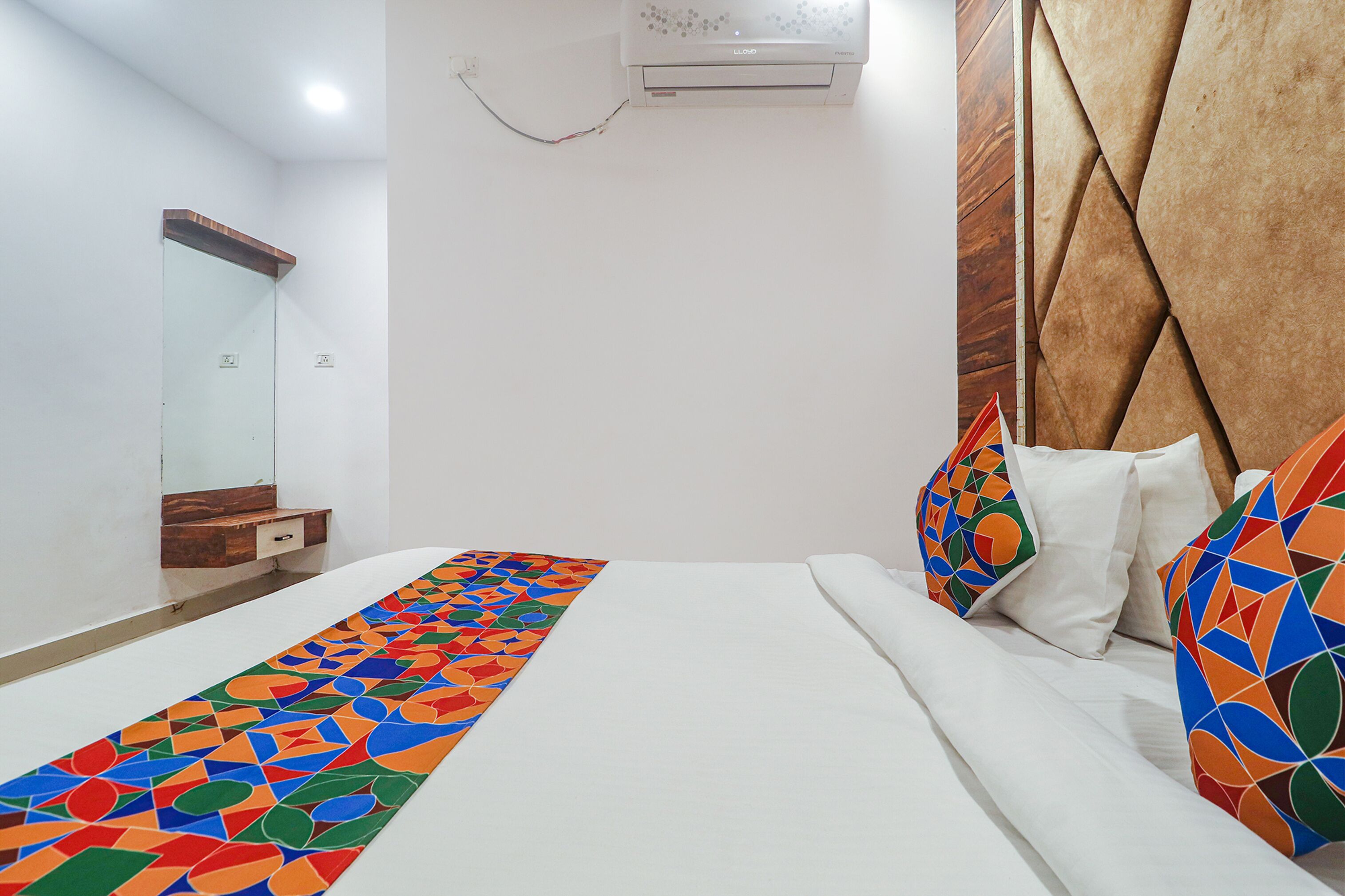 Une chambre d’hôtel avec un lit, un miroir, une tête de lit en bois et un tapis coloré.