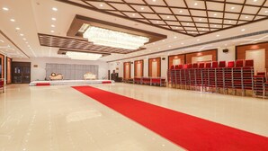 A spacious hall with a red carpet leading to a stage, rows of red chairs, and a modern chandelier. - Fabhotel Double Tree (Hyderabad)