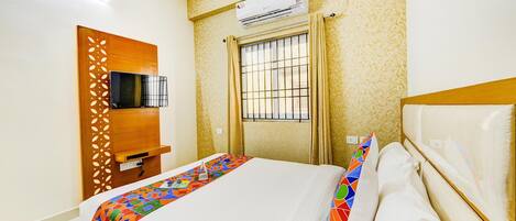 A hotel room with a bed, a television mounted on the wall, an air conditioner, and a window with bars.