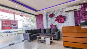 A modern reception area with a sofa, a wooden desk, and a wall with decorative roses. - Fabhotel The Orient (Haridwar)