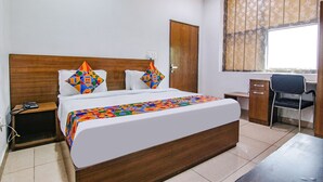 A hotel room with a large bed, a desk, a chair, and a window with curtains. - Fabhotel The Orient (Haridwar)