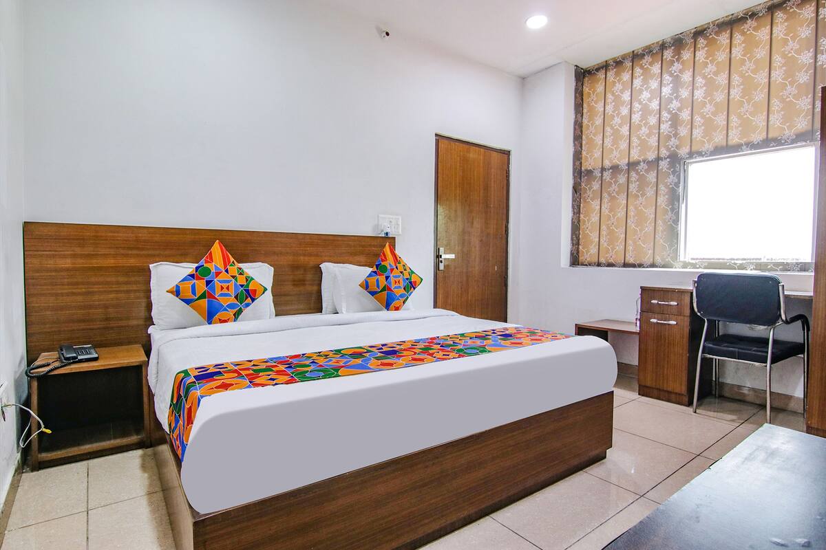 A hotel room with a large bed, a desk, a chair, and a window with curtains.