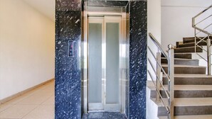 An elevator with a digital display, adjacent to a staircase with metal railings and a handrail. - Fabhotel The Orient (Haridwar)