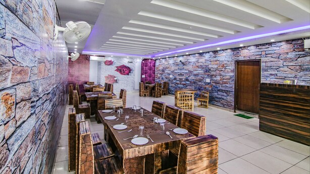 A restaurant with wooden tables and benches, stone walls, and a modern ceiling design. - Fabhotel The Orient (Haridwar)