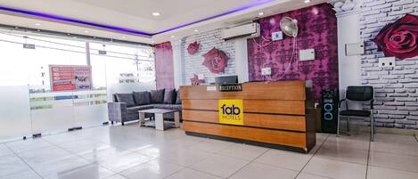 A hotel reception area with a reception desk, a sofa, and a fan.