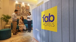 A reception area with a 'fab hotels' sign, a blue wall, a green sofa, and framed pictures on the wall. - Fabhotel Benchmark (Indore)