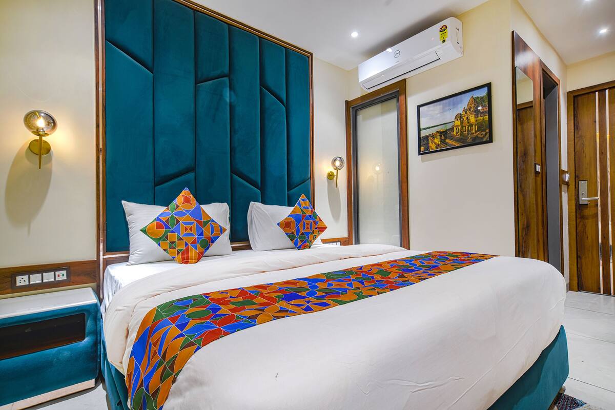 A hotel room with a large bed, a teal headboard, a colorful bedspread, and a painting on the wall.