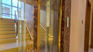 A modern elevator with a marble wall, a glass panel, and a wooden door. - Fabhotel Benchmark (Indore)