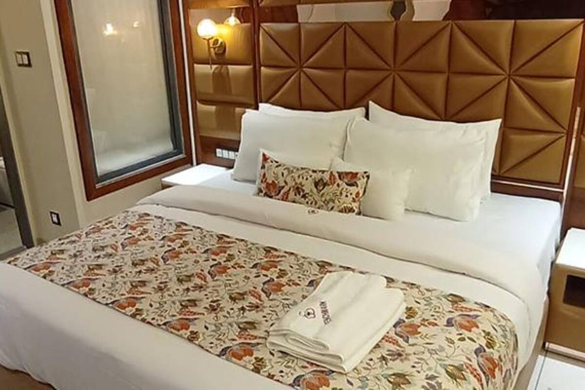 A bed with a floral bedspread, a headboard with a geometric pattern, and a bedside table with a lamp.