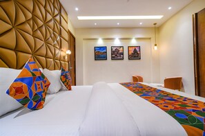 A hotel room with a large bed, a decorative headboard, and a long table with a colorful runner. - Fabhotel Benchmark (Indore)