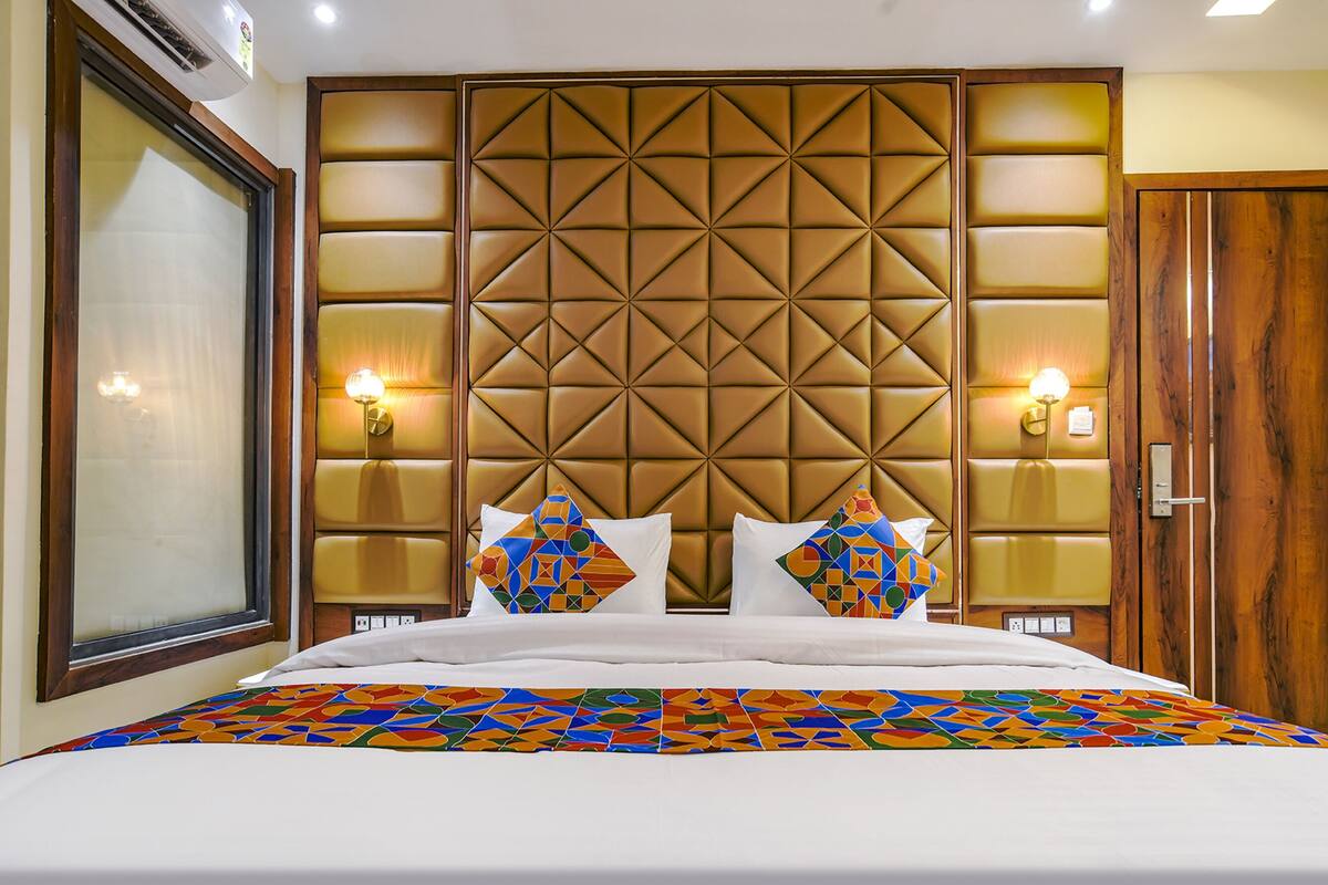 A hotel room with a large bed, a wooden headboard with a geometric pattern, two wall-mounted lights, and a wooden wardrobe.
