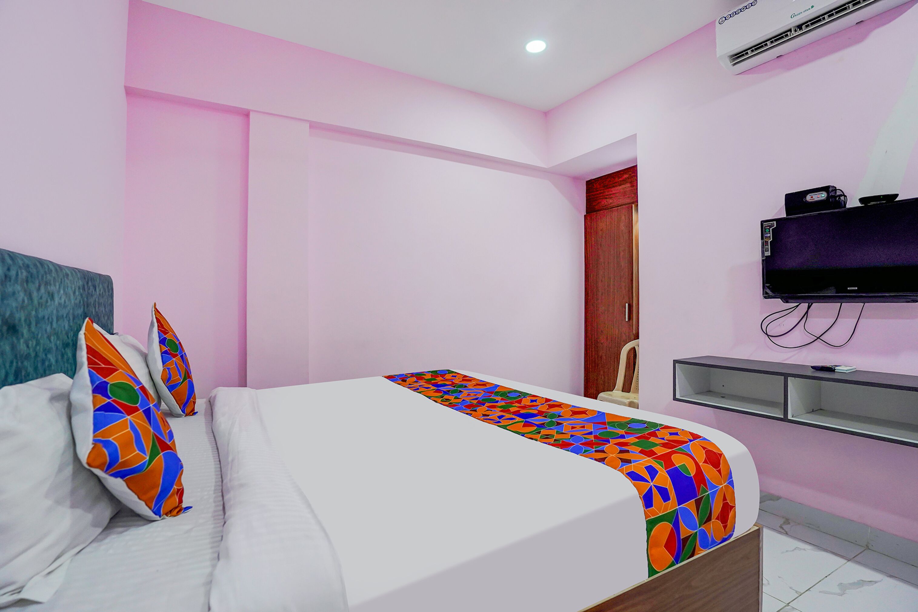 A bedroom with a bed, pillows, a TV, and a wall-mounted shelf.