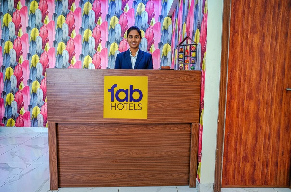 Una recepción con un letrero de 'fab hotels', un mostrador de madera y una pared de fondo con un estampado de plumas de colores.