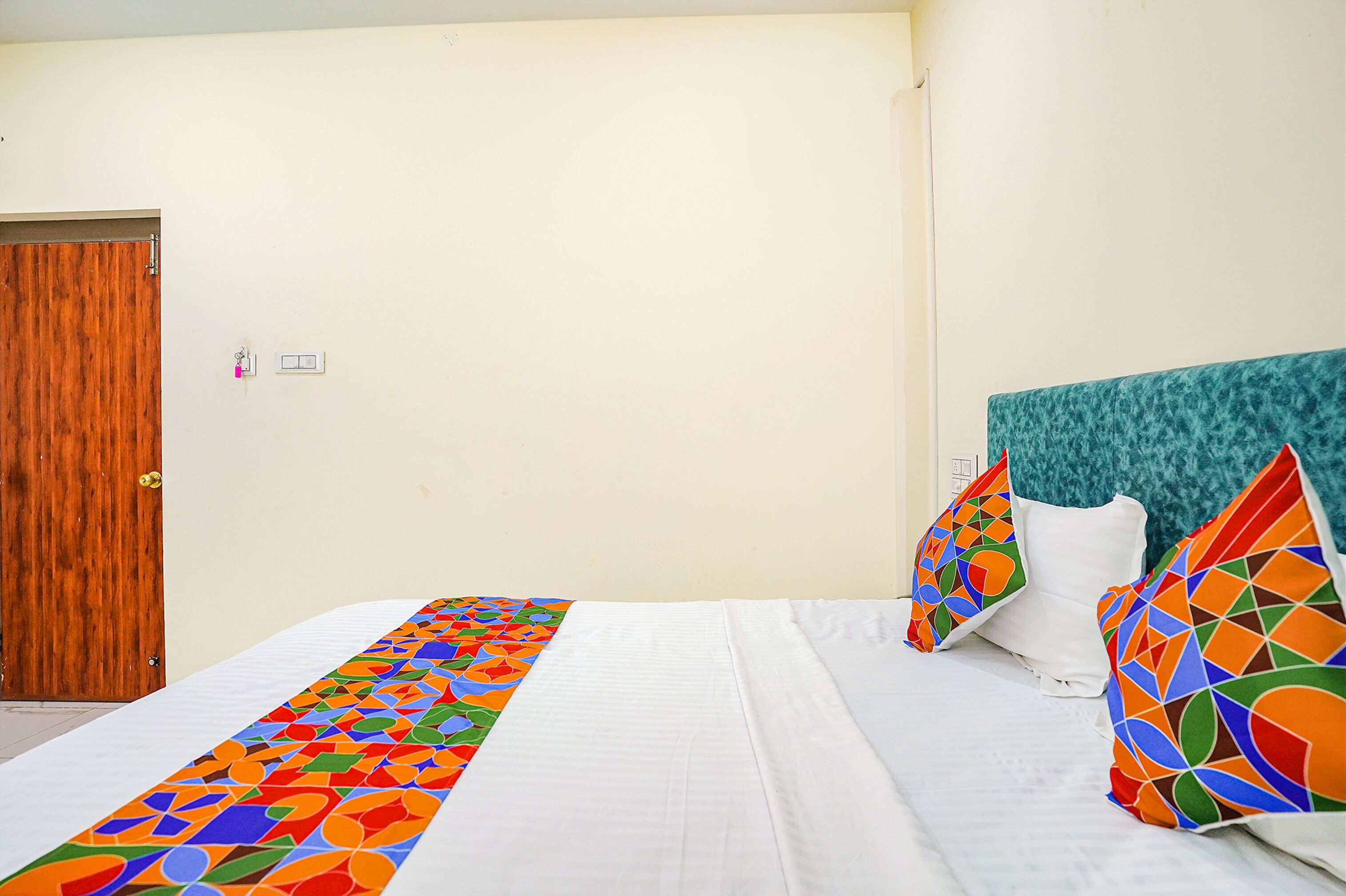 A hotel room with a bed, a wooden door, and a teal headboard.