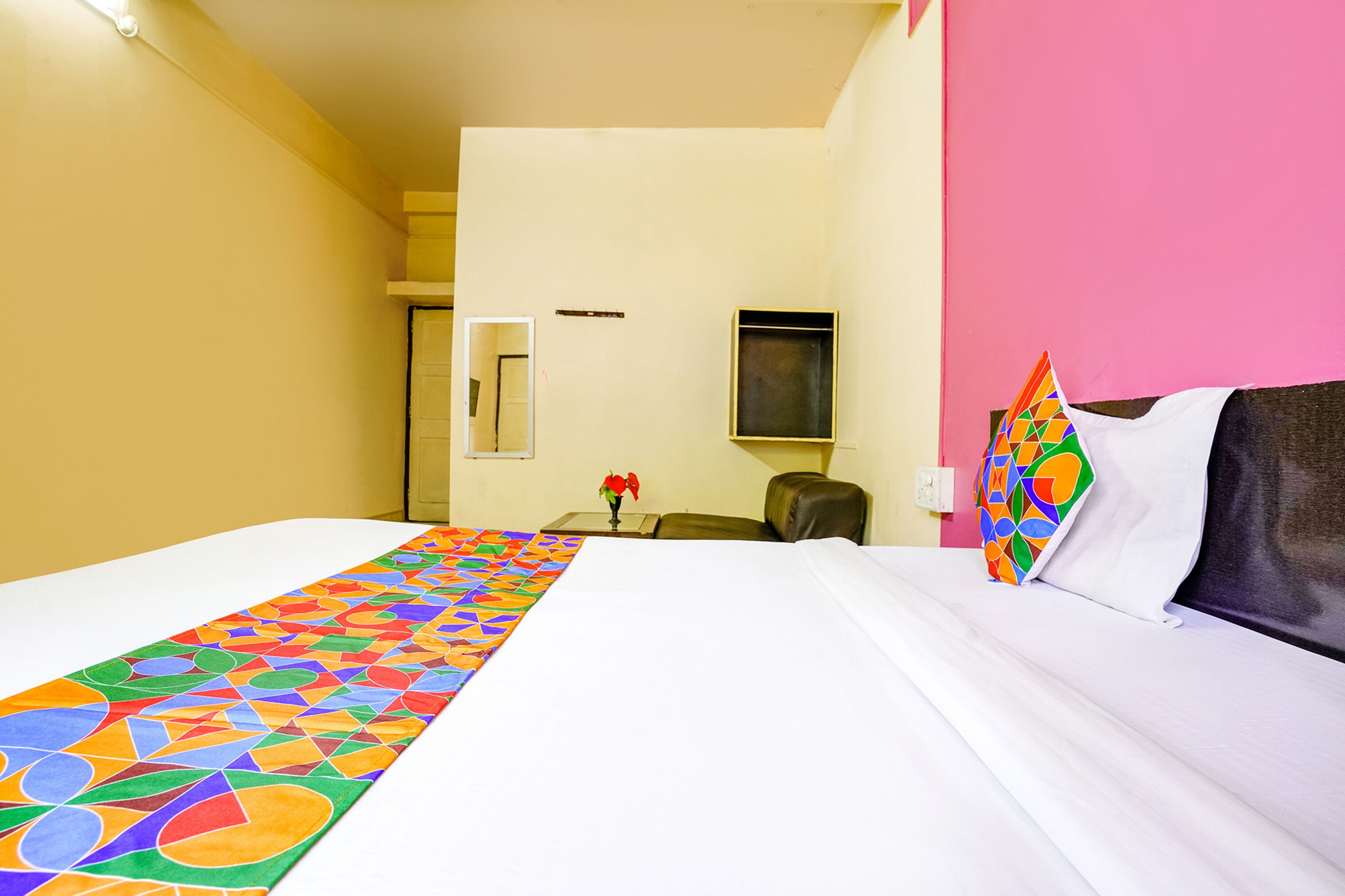 A hotel room with a large bed, a desk, a chair, and a pink wall.