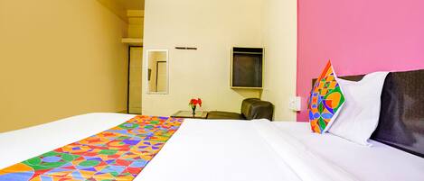 A hotel room with a large bed, a desk, a chair, and a pink wall.
