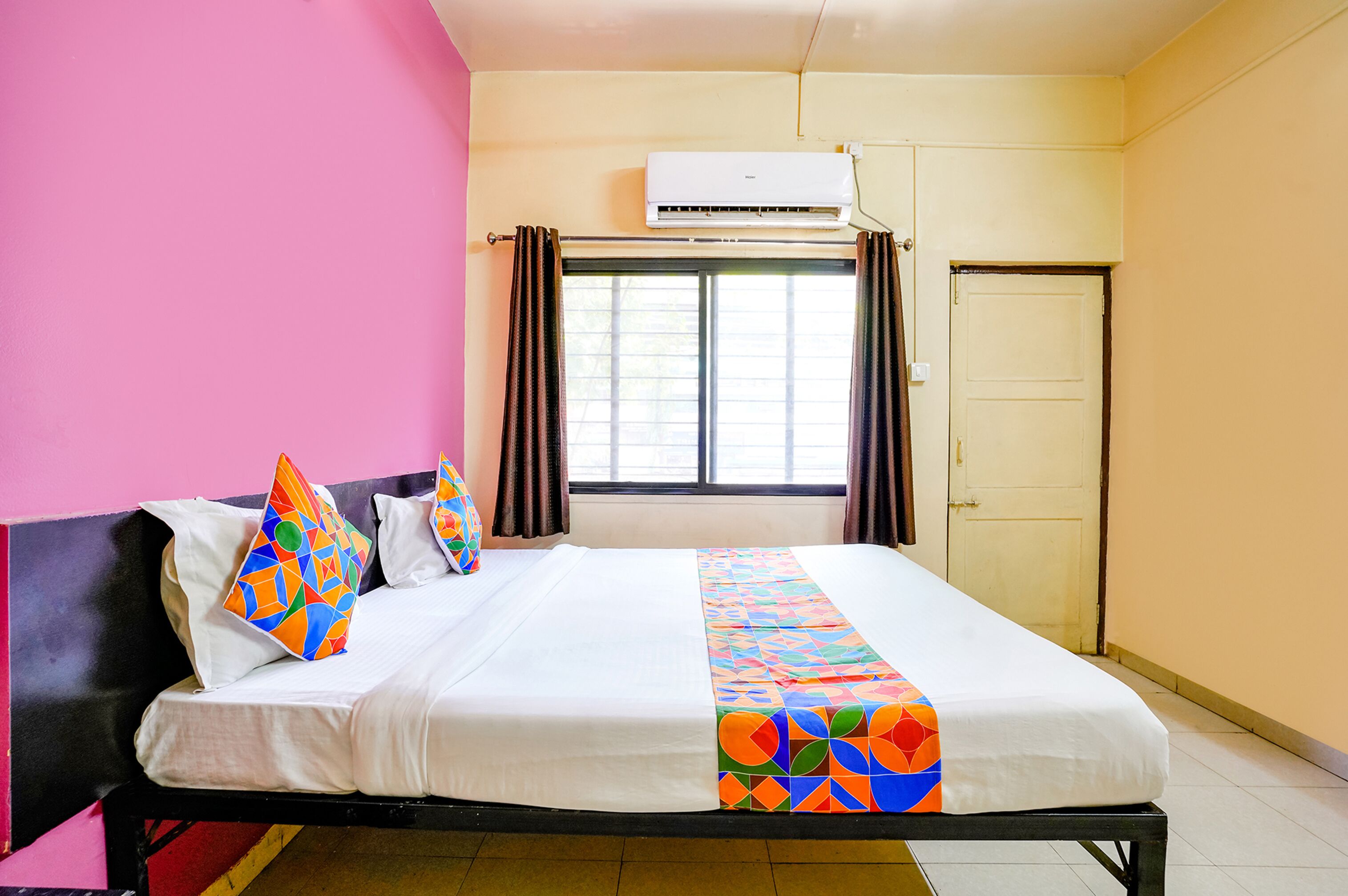 Une chambre d’hôtel avec un lit, une fenêtre avec des rideaux, un appareil de climatisation et une porte.