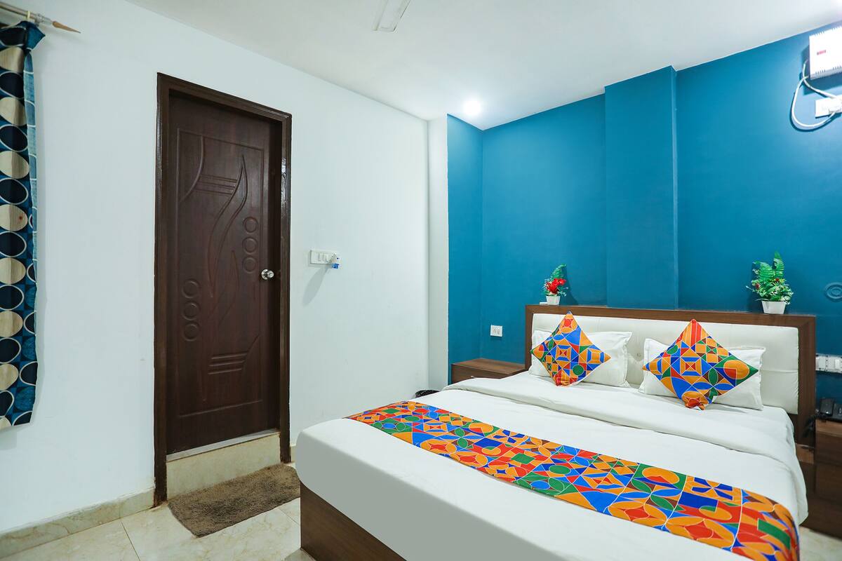 Un dormitorio con una cama, una puerta de madera, una pared azul y una planta pequeña en la mesita de noche.