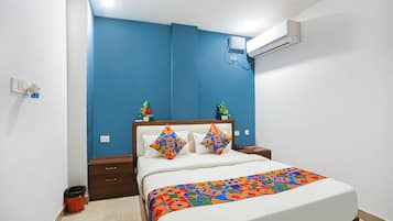 A bedroom with a bed, a nightstand, a trash bin, and a wall-mounted air conditioner.