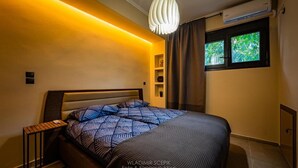 A modern bedroom with a bed, bedside tables, a hanging light fixture, a window with a view, and built-in shelves. - Sehr Schöne und Moderne Ferienwohnung Lighthouse (Loutraki)