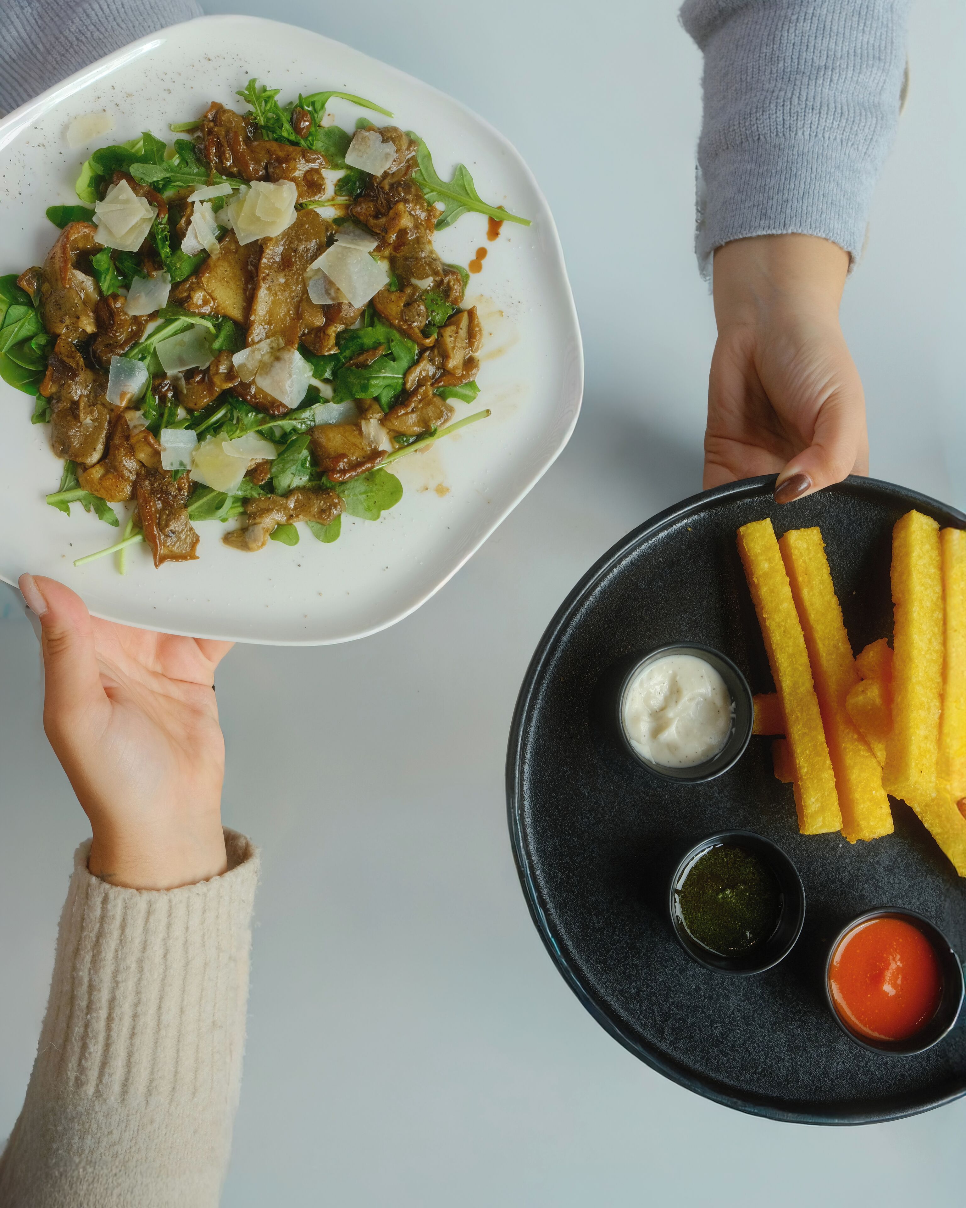 Un plato de carne con verduras y queso, y una bandeja con papas fritas y dos salsas para mojar.