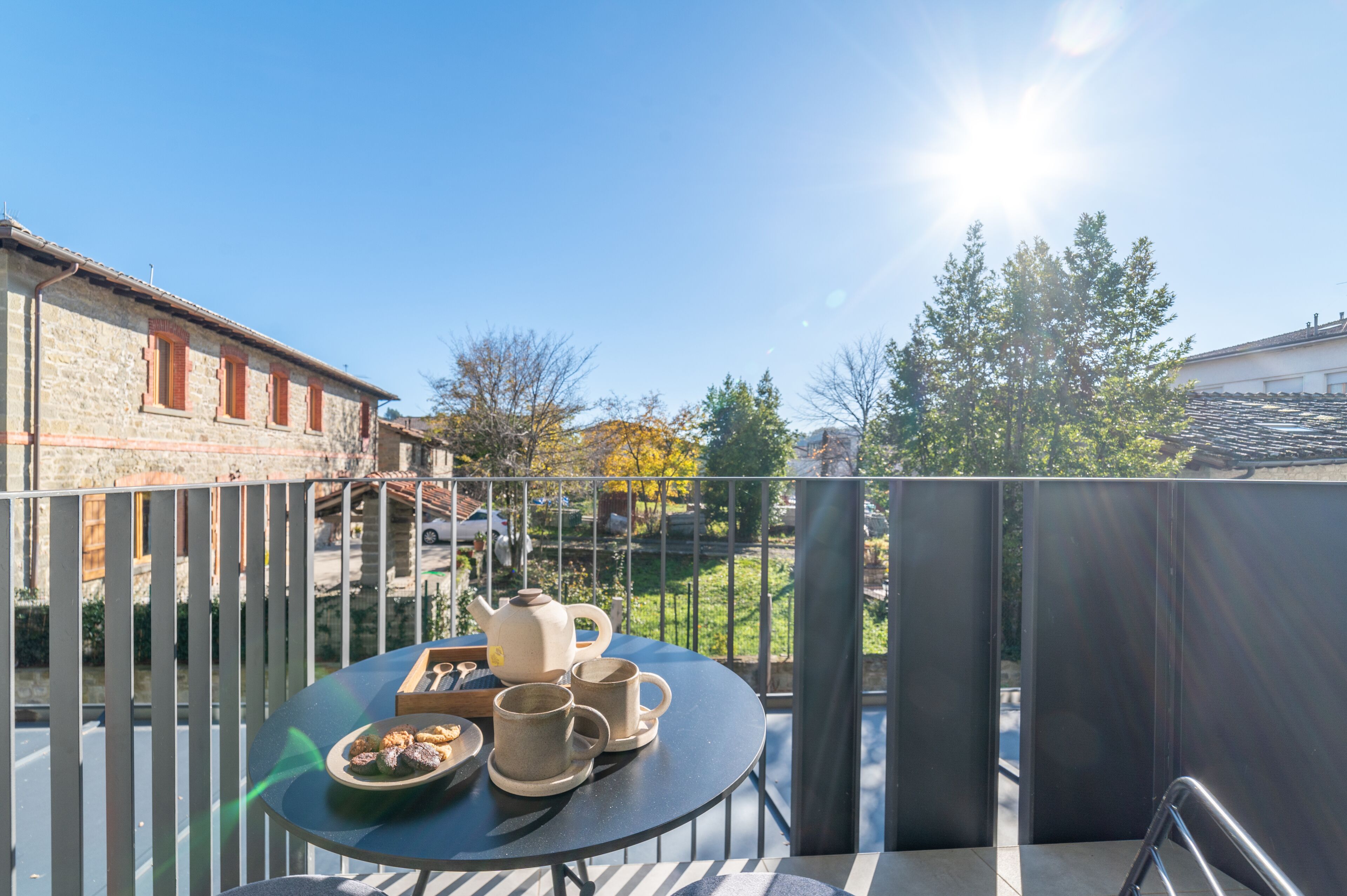 A balcony with a table set for tea, overlooking a street with parked cars and buildings.