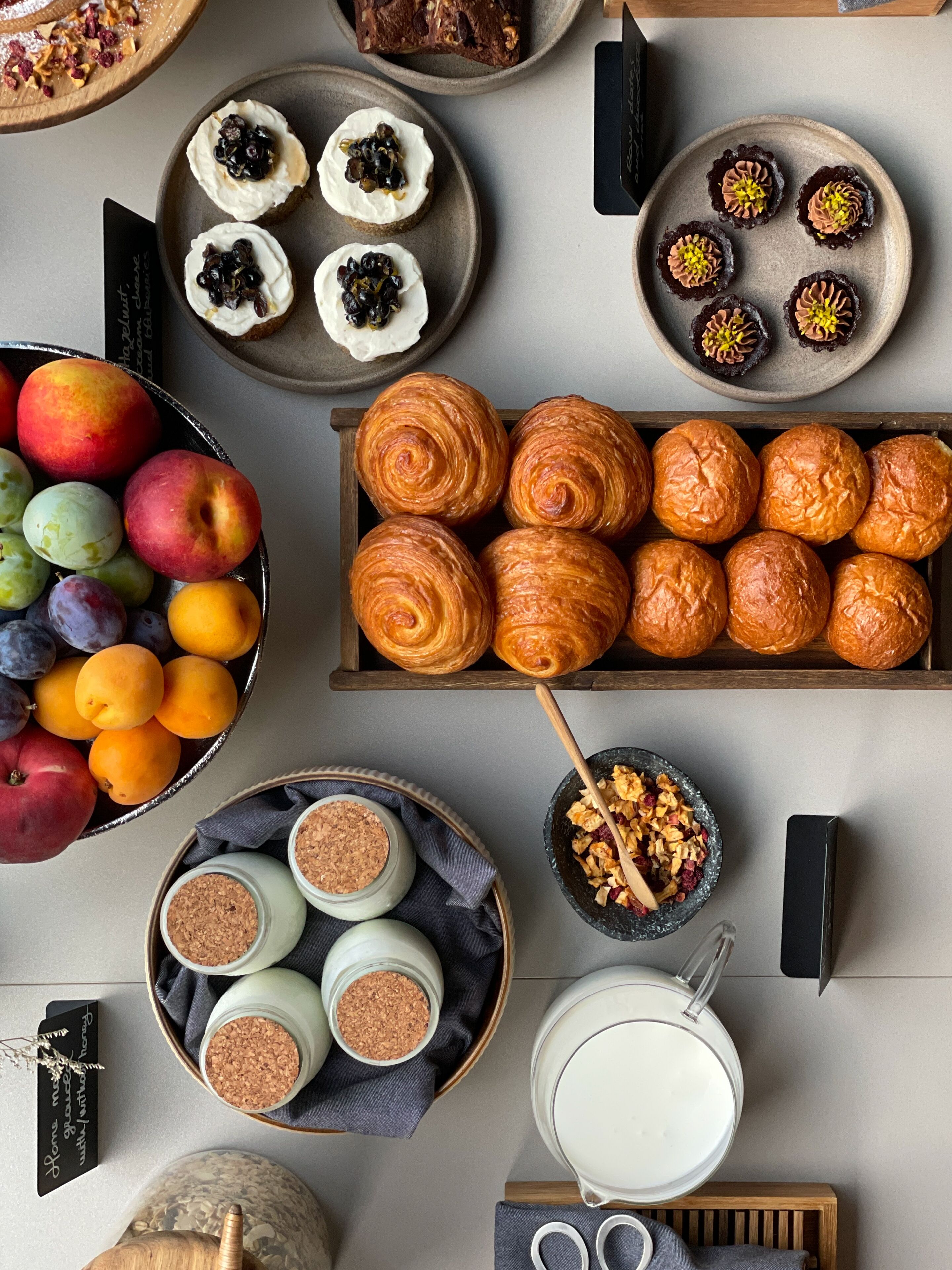 Diversas opciones de pastelería, frutas y una jarra de leche sobre una mesa.